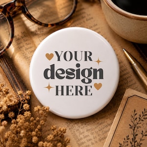 Könnte beinhalten: Ein weißer Button mit dem Text "YOUR design HERE" in Dunkelgrau, verziert mit goldenen Herzen und Sternen. Er liegt auf einem Vintage-Papierhintergrund, mit Brille und Stift in der Nähe.
