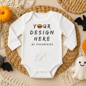 May include: White baby bodysuit with long sleeves, featuring the text "YOUR DESIGN HERE" and a pumpkin graphic. The image includes Halloween-themed decorations like pumpkins, bats, and a ghost.