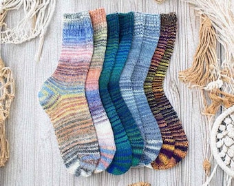 May include: Six pairs of colorful striped socks in a variety of blue, green, orange, and brown hues. The socks are arranged in a semi-circle on a light wood surface.