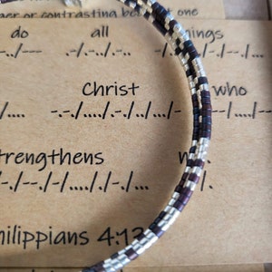 May include: A brown and silver beaded bracelet with the text "Christ strengthens" and "Philippians 4:13" on a brown paper background.