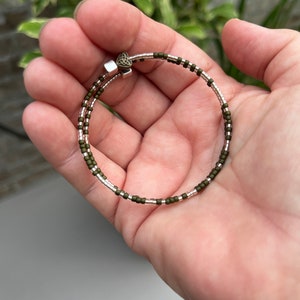 Könnte beinhalten: Ein Armband mit zwei Reihen aus grünen und silbernen Perlen. Das Armband hat einen silbernen Verschluss mit einem keltischen Knotendesign.