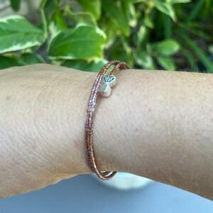 May include: A double-wrap bracelet made of small, brown beads with a silver charm in the shape of a heart with a Celtic knot design.