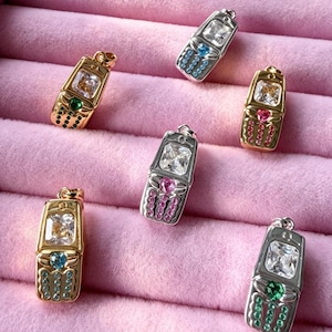 May include: Six metallic pendants shaped like vintage flip phones, each featuring a large rectangular clear stone at the top, a small heart-shaped stone in the center, and rows of tiny colored accent stones representing a keypad.