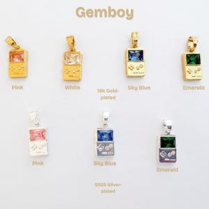 May include: A collection of Gemboy pendants shaped like handheld game consoles. The top row features 18k gold-plated pendants with pink, white, sky blue, and emerald rectangular gemstones. The bottom row shows S925 silver-plated pendants in pink, sky blue, and emerald.