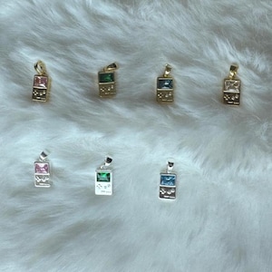 May include: A collection of seven rectangular pendants shaped like handheld video game consoles. Four pendants are gold-toned with pink, green, dark blue, and clear stones. Three pendants are silver-toned with pink, green, and blue stones.