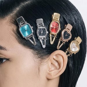 May include: Five hair clips featuring miniature analog watch faces in various shapes and colors. The collection includes square, oval, and heart-shaped designs in silver, gold, and rose gold tones with blue, black, red, and white dials.
