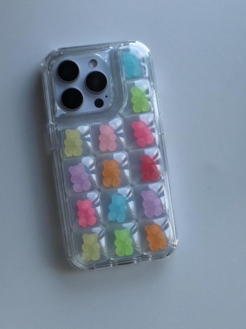 May include: Clear phone case with a colorful gummy bear design. The case features a grid pattern filled with various colored gummy bear shapes, including blue, green, pink, orange, and purple. The phone's camera lenses are visible at the top.