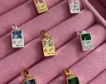 May include: Seven rectangular pendants shaped like handheld video game consoles, featuring metallic gold or silver finishes and inset with colorful, faceted rectangular gemstones in pink, blue, green, and clear tones, each with a small top bail.
