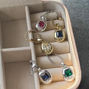 Puede incluir: Una colección de colgantes de piedras preciosas en un estuche de joyería. Los colgantes presentan piedras de varios colores, incluyendo rojo, azul, verde y transparente, engastadas en monturas de oro y plata. Cada colgante está unido a una delicada cadena.