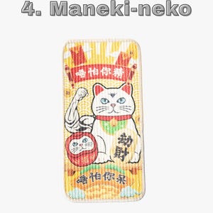 Może przedstawiać: Prostokątna naszywka z białym kotem Maneki-neko z niebieskimi oczami, czerwoną obrożą i zielonym śliniakiem. Kot jest przedstawiony z uniesioną ręką i znajduje się obok czerwonej lalki Daruma. Tło jest ż&oacute;łte z chińskim tekstem i słowami "Maneki-neko" u g&oacute;ry.