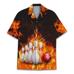 Puede incluir: Camisa de manga corta con botones con temática de bolos. La camisa presenta un gráfico de bolos y una bola de bolos roja sobre un fondo de llamas. La camisa tiene un fondo negro con llamas naranjas y amarillas.
