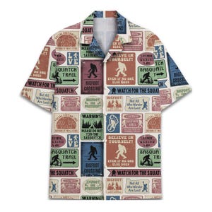 May include: Short-sleeved shirt with a Bigfoot-themed design. The shirt features a collage of signs with phrases such as "Bigfoot Crossing," "Watch for the Squatch," and "Believe in Yourself!" in various colours.