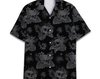 Peut inclure: Une chemise à manches courtes boutonnée noire avec un motif répétitif de crânes gris, de feuilles de palmier tropicales et de fleurs. Le vêtement présente un col classique, un ourlet droit et des boutons blancs sur la patte de boutonnage.
