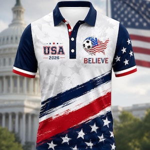 Può includere: Polo bianco con un design patriottico. Presenta il testo "USA 2026" e "BELIEVE", insieme alla bandiera americana, stelle e strisce rosse, bianche e blu. Le maniche sono blu navy con finiture rosse e bianche.