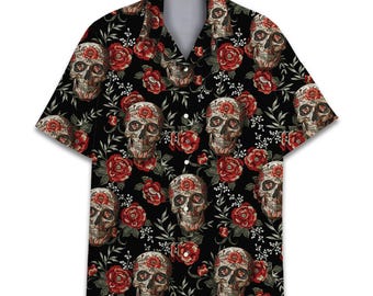 Peut inclure: Une chemise à manches courtes boutonnée avec un fond noir et un motif répétitif de crânes humains et de roses rouges. Les crânes sont représentés dans des tons beige et marron, entremêlés de feuilles vertes et de petits accents floraux blancs.