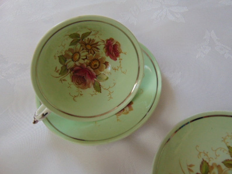 Paragon footed cup and 2 saucers in green floral small brown mark on the cup