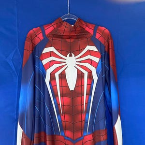 May include: A blue and red spandex costume with a white spider design on the chest. The costume has a high neck and long sleeves.