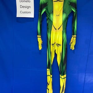 Op de afbeelding: Een groen en geel vol-body pak met een zwart ontwerp. Het pak hangt aan een hanger tegen een blauwe achtergrond. De tekst "Domello Design Custom" is zichtbaar op een wit label.