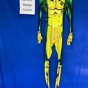 Op de afbeelding: Geel en groen spandex jumpsuit met een stripfiguurontwerp. Het personage heeft een grote X op zijn borst.