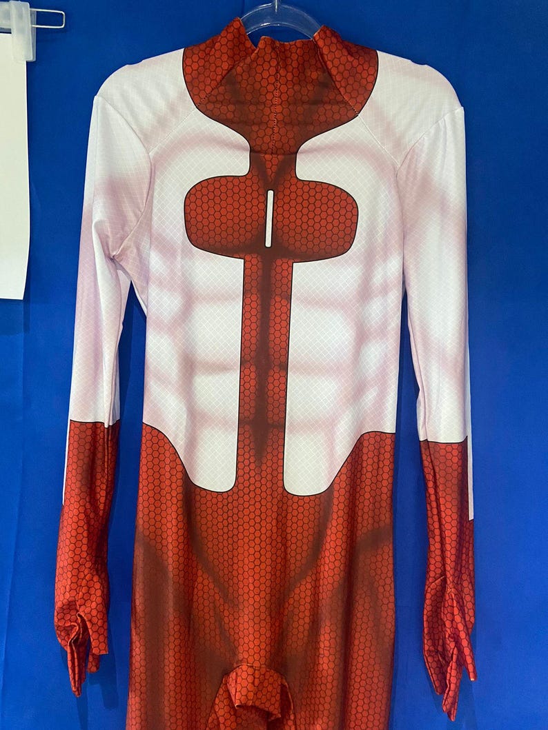 Puede incluir: Un traje de cuerpo entero rojo y blanco con un patr&oacute;n de panal. El traje tiene cuello alto y mangas largas.