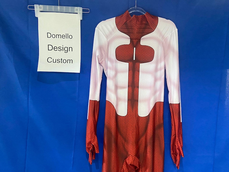 Puede incluir: Un body de spandex rojo y blanco con un patr&oacute;n de panal. El body tiene cuello alto y mangas largas. El texto "Domello Design Custom" est&aacute; en un cartel blanco.