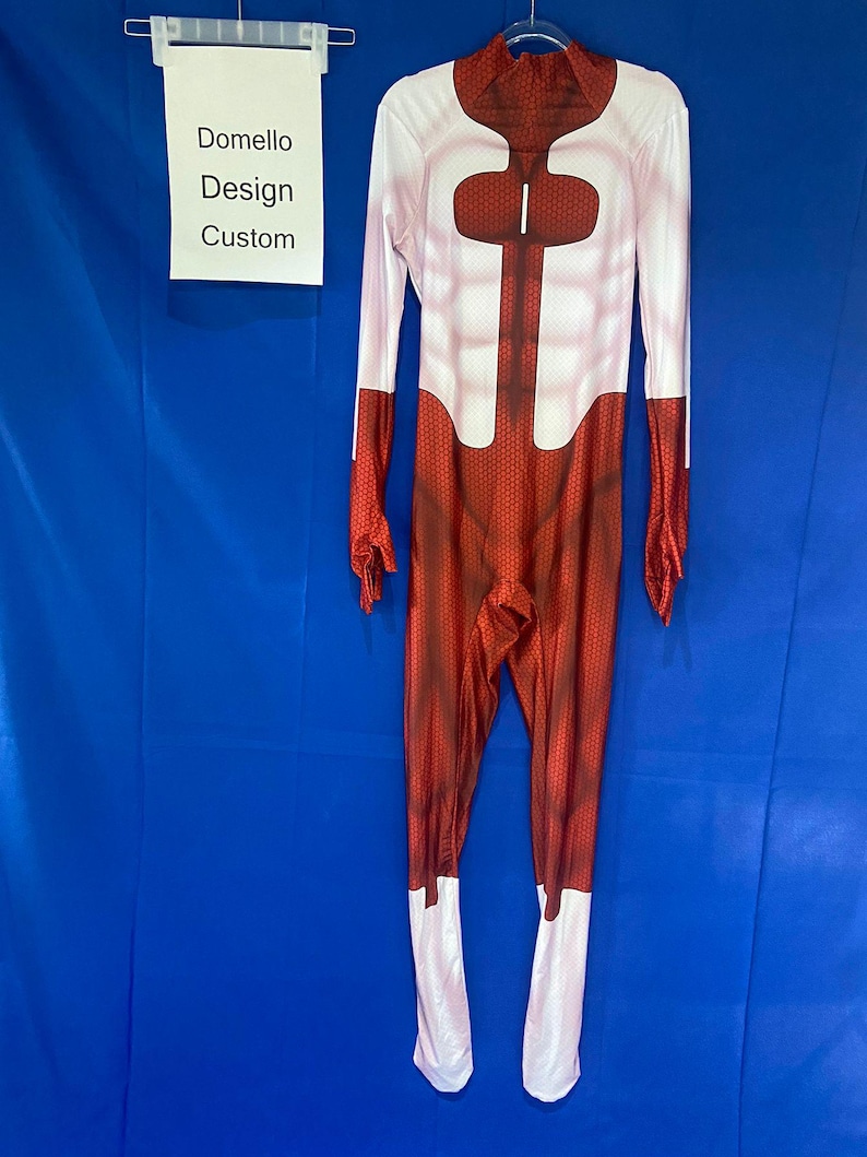 Puede incluir: Traje de cuerpo entero rojo y blanco con un patr&oacute;n de panal. El traje tiene cuello alto y mangas largas. El traje est&aacute; hecho de un material el&aacute;stico. El traje tiene un panel de pecho blanco con un patr&oacute;n de panal rojo. El traje tiene un panel blanco en las piernas. El traje est&aacute; colgado en una percha. El texto "Domello Design Custom" est&aacute; en una etiqueta blanca.