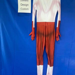 Puede incluir: Un traje de cuerpo entero rojo y blanco con un patr&oacute;n texturizado. El traje tiene mangas largas y cuello alto. El traje est&aacute; hecho de un material el&aacute;stico. "Domello Design Custom" est&aacute; escrito en un cartel blanco.