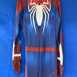 May include: A blue and red spandex jumpsuit with a white spider logo on the back. The suit has a zipper down the front and a red spider web pattern on the arms and legs.