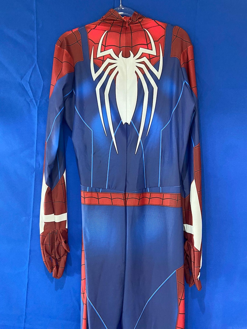 May include: A blue and red spandex jumpsuit with a white spider logo on the back. The suit has a zipper down the front and a red spider web pattern on the arms and legs.