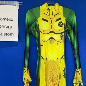 Op de afbeelding: Een geel en groen spandex pak met een stripfiguurontwerp. Het personage heeft een geel lichaam met zwarte lijnen en een groene X op de borst. Het pak heeft lange mouwen en een hoge hals.