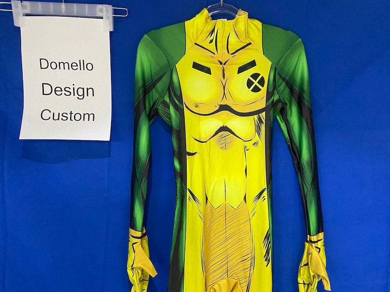 Op de afbeelding: Een geel en groen spandex pak met een stripfiguurontwerp. Het personage heeft een geel lichaam met zwarte lijnen en een groene X op de borst. Het pak heeft lange mouwen en een hoge hals.