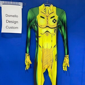 Op de afbeelding: Een geel en groen spandex pak met een zwarte X op de borst. Het pak heeft een bedrukt ontwerp van een gespierde figuur. De tekst "Domello Design Custom" staat op een wit kaartje dat boven het pak hangt.
