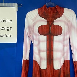 Puede incluir: Body blanco de manga larga con un patr&oacute;n de panal de abeja rojo en el pecho y el torso. El texto "Domello Design Custom" est&aacute; en un cartel blanco.