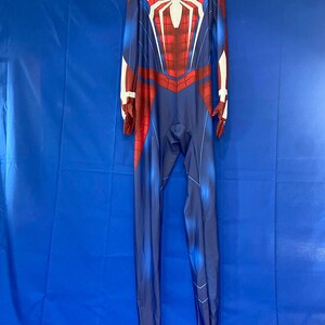 May include: A blue and red spandex jumpsuit with a white spider design on the chest. The suit has a zipper in the back and a high neck.
