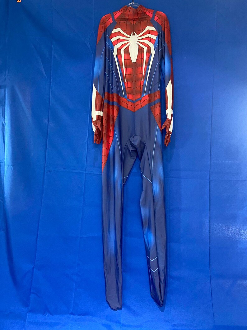May include: A blue and red spandex jumpsuit with a white spider design on the chest. The suit has a zipper in the back and a high neck.