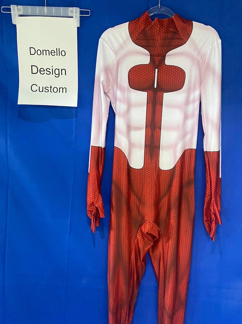 Puede incluir: Un traje de cuerpo entero rojo y blanco con un patr&oacute;n de panal. El traje tiene cuello alto y mangas largas. El traje est&aacute; hecho de un material el&aacute;stico. El traje tiene una pieza de pecho roja con una franja blanca en el centro. El traje est&aacute; colgado en una percha contra un fondo azul. El texto "Domello Design Custom" es visible en un cartel blanco.