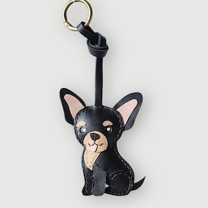 Può includere: Portachiavi Chihuahua in pelle nera con anello color oro. Il cane ha orecchie color beige e una macchia beige sul petto. Il portachiavi è fatto a mano e presenta il testo "SC CRAFT" in basso.