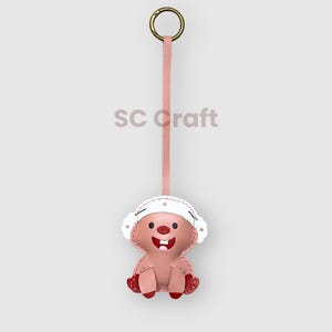 May include: A pink leather keychain in the shape of a cartoon character with a white hat and red accents. The keychain has a gold ring and a pink strap. The text "SC craft" is visible.