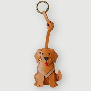 May include: A brown leather dog keychain with a brass-colored clasp. The dog is in a sitting position with a red tongue. The keychain has the text "SC CRAFT" at the bottom.