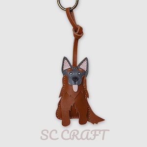 May include: A brown and gray leather dog keychain featuring a German Shepherd design with a light-colored tongue, pointed ears, and a metal ring attachment. The text SC CRAFT is printed in a light gray font at the bottom of the image.