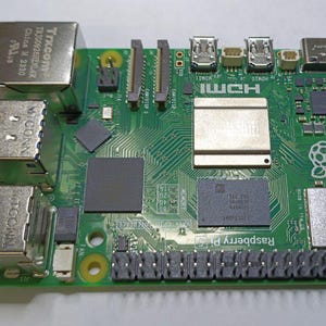 Puede incluir: Una placa de ordenador Raspberry Pi verde con un disipador de calor plateado, dos puertos USB, un puerto Ethernet y una ranura para tarjeta micro SD.
