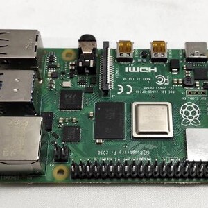 Könnte beinhalten: Eine grüne Raspberry Pi Computerplatine mit einer Vielzahl von Anschlüssen und Steckverbindern, darunter HDMI, USB und Ethernet. Die Platine hat einen kleinen, weißen Aufkleber mit dem Raspberry Pi Logo. Der Text auf der Platine lautet "FCC 1D 2ABCS-87140 IC 20453-RP14E FC CE Mode in The UK HDMI GLOBAL EK Raspberry Pi 2018".