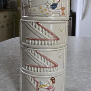 May include: A stack of four ceramic containers. Each container is a light beige color and features a different embossed scene. The scenes depict a person in bed, a staircase, and a person carrying a tray. The staircase has red accents.