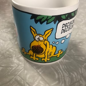 May include: A white ceramic mug with a blue background and a cartoon yellow dog with a thought bubble that says "Decisions, Decisions".