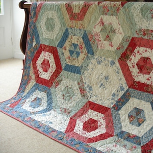 Könnte beinhalten: Eine Steppdecke mit einem geometrischen Muster in Rot-, Blau- und Weißtönen. Die Steppdecke ist aus Stoff mit Blumenmuster gefertigt.