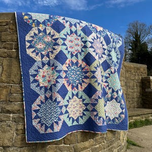 May include: A blue and white patchwork quilt with a starburst pattern. The quilt is hanging on a stone wall.