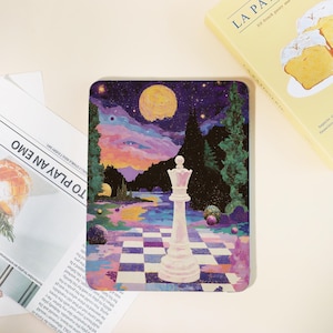 Peut inclure: Un dessous de verre carré avec un paysage surréaliste représentant une reine d'échecs blanche sur un échiquier. L'œuvre comprend une pleine lune, des arbres et une rivière. Le dessous de verre est à côté d'un livre et d'un journal.
