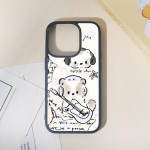 May include: A white phone case with a dark gray border featuring a cartoon illustration of a dog playing a guitar. The case has additional drawings of dogs, stars, and text. The text includes the words "you", "shine for", and "must be a person."
