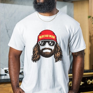 May include: White t-shirt featuring a graphic of a man with long brown hair, a beard, and sunglasses. The man is wearing a red bandana with the words "MACHO MAN" printed on it. The shirt is a classic crew neck.