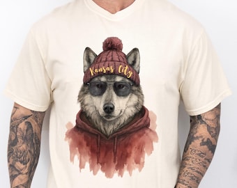 Könnte beinhalten: Cremefarbenes T-Shirt mit einer Aquarellillustration eines Wolfes, der eine weinrote Mütze mit dem Text "Kansas City" in goldfarbenen Buchstaben, eine schwarze Sonnenbrille und einen weinroten Kapuzenpullover trägt. Das Fell des Wolfes ist grau und weiß.